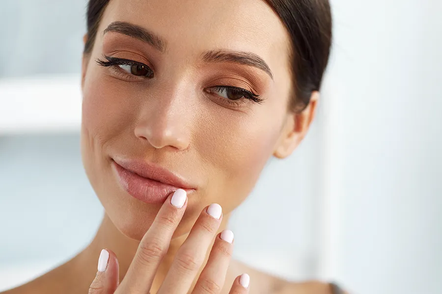 Aesthetic-Dermal-Fiilers-Clinic A beautiful brunette touches her faces. Get aesthetic dermal fillers from Brandi Terra, NP at Oak & Stone Wellness in East San Diego.