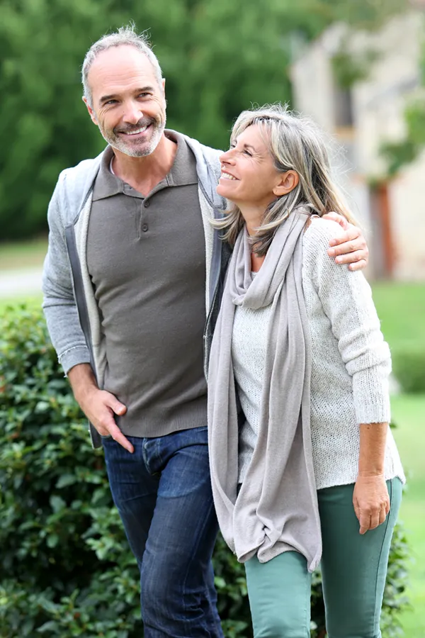 Bioidentical-Hormone-Therapy-Treatment A mature couple in gray toned clothes and jeans walk happily outside, happy with their successful bioidentical hormone treatments from Brandi Terra, NP at Oak & Stone Wellness in East San Diego.