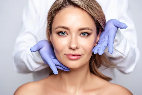 Botox-Doctor Close up of a woman's face with a doctor wearing rubber gloves standing behind her holding his hands around her face to show the amazing Botox Cosmetic treatment from Brandi Terra, NP at Oak & Stone Wellness in East San Diego.