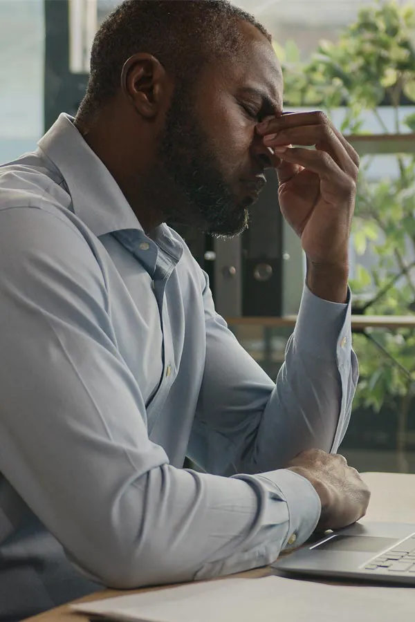 Chronic-Fatigue-Treatment A black man rubbing the top of his nose at his desk, in need of chronic fatigue treatment from Brandi Terra, NP at Oak & Stone Wellness in East San Diego.
