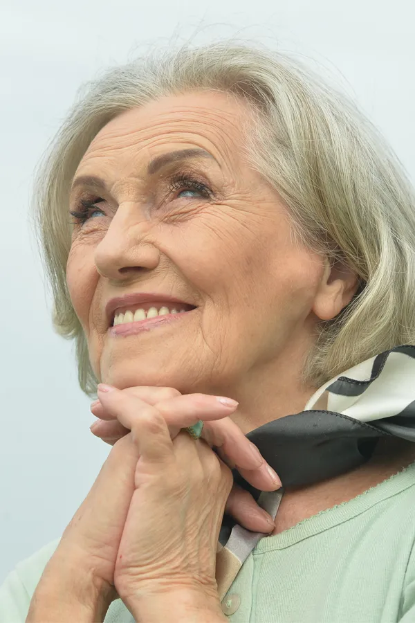 Hot-Flashes-and-Night-Sweats-Treatments An older woman holds her hands together under her chin and looks up at a cool sky smiling. Get treatment for hot flashes and night sweats from Brandi Terra, NP at Oak & Stone Wellness in East San Diego.