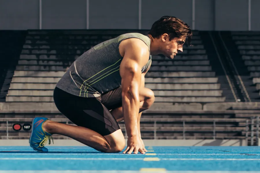 Lean-Muscle-and-Recovery-Clinic A white man kneels at the starting line on a track, determined to do his best. Get treatment for lean muscle loss and recovery from Brandi Terra, NP at Oak & Stone Wellness in East San Diego.
