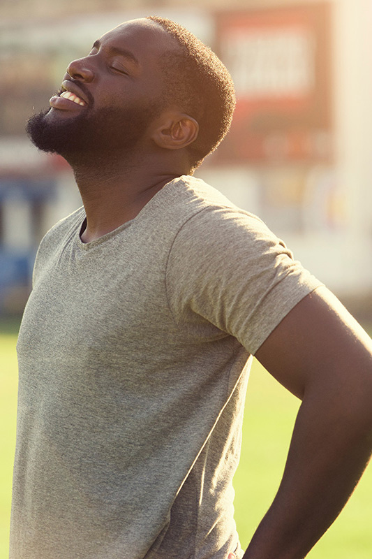 Lean-Muscle-and-Recovery-Treatment A black man in a gray t-shirt and smiles, looking up with closed eyes after a satisfying workout. Get treatment for lean muscle loss and recovery from Brandi Terra, NP at Oak & Stone Wellness in East San Diego.