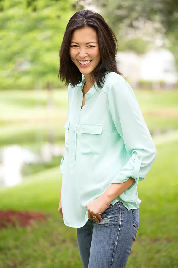 Perimenopause-Treatment A middle-aged brunette woman in a light green button-up shirt stands outside smiling, happy with her perimenopause treatment from Brandi Terra, NP at Oak & Stone Wellness in East San Diego.