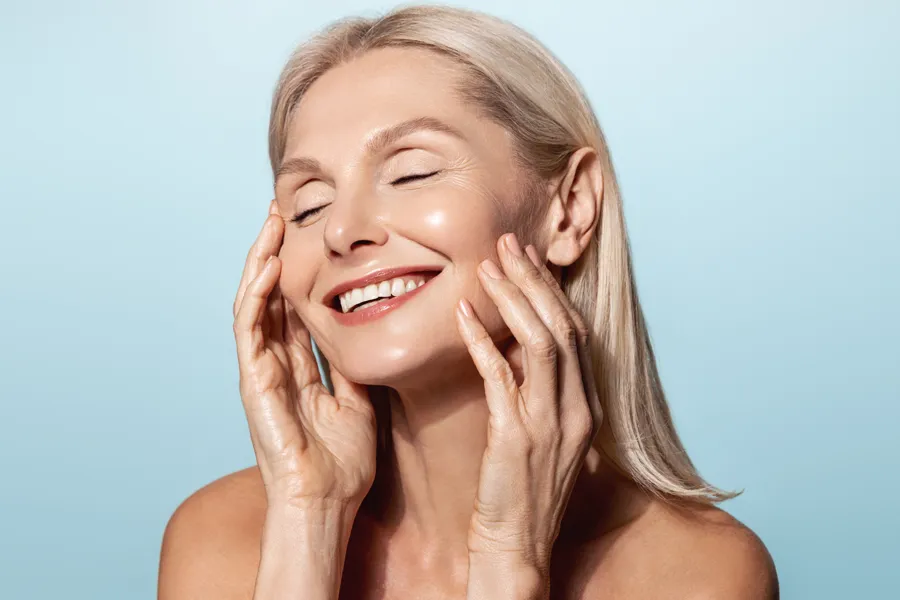 Radiofrequency-Microneedling-for-Face-and-Jawline-Clinic A woman with a smooth, tight jawlline smiles and holds her face. Schedule Radiofrequency Microneedling for Face and Jawline Skin Treatment from Brandi Terra, NP at Oak & Stone Wellness in East San Diego.