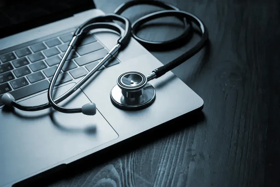 Telemedicine-Doctor An open laptop with a stethoscope lying on it on a wooden table, symbolizing telemedicine care from Brandi Terra, NP at Oak & Stone Wellness in East San Diego.