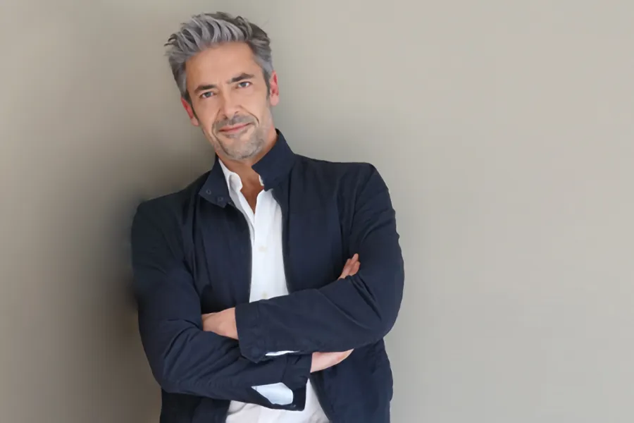 Testosterone-Low-T-Solutionsn-Clinic A middle-aged man in a white shirt and dark blue jacket leans against a gray wall smiling. Get testosterone for Low T from Brandi Terra, NP at Oak & Stone Wellness in East San Diego.