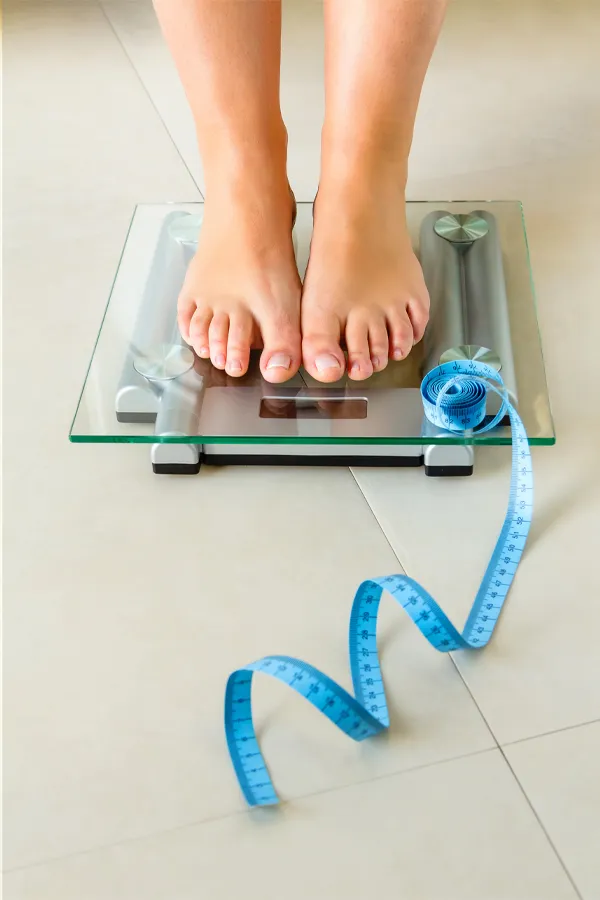 Weight-Loss-Resistance-Treatment Close-up of a woman's feet standing on a scale, with measuring tape by her toes, getting treatment for weight loss resistance from Brandi Terra, NP at Oak & Stone Wellness in East San Diego.